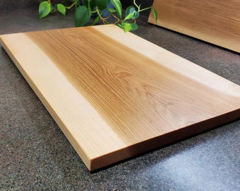 May include: A rectangular wooden chopping board with a light wood border and a darker wood centre. The board is made from two different types of wood, creating a unique and beautiful design.