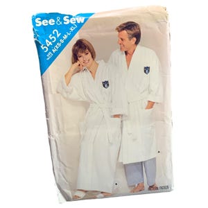 May include: A vintage sewing pattern titled "See & Sew 5452" featuring a couple wearing white bathrobes with a crest on the chest. The pattern includes sizes XS to XL. The packaging is slightly worn.
