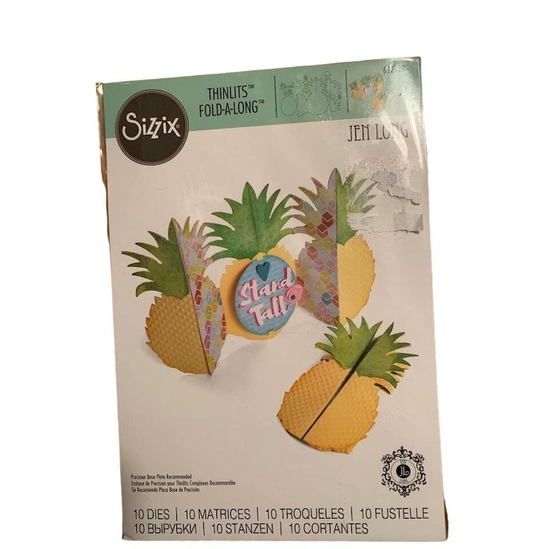 May include: A Sizzix Thinlits Fold-A-Long die set with pineapple designs. The packaging includes the text "Stand Tall" and "Jen Long". The set contains 10 dies, matrices, troqueles, fustelle, vyrubki, stanzen, and cortantes.