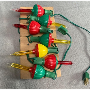 May include: A string of Christmas lights with red, yellow and green bulbs. The lights are connected to a cord with a plug on the end.