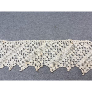 May include: Cream-colored crochet lace trim with a scalloped edge. The lace features an openwork design with small, evenly spaced holes. The trim appears to be vintage or antique, with some slight discoloration.