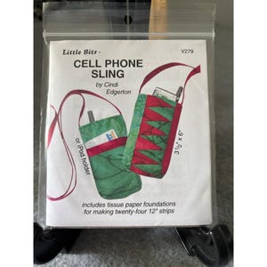 May include: A clear plastic bag containing a sewing pattern for a cell phone sling. The pattern features a green and red fabric design, with the text "CELL PHONE SLING" and "by Cindi Edgerton". The sling measures 3.5" x 6".