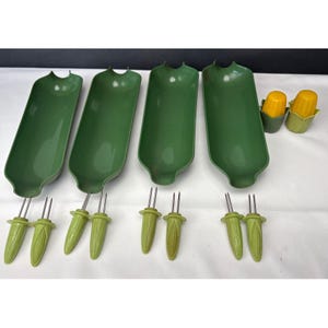 May include: A set of four elongated green plastic corn-on-the-cob serving dishes, eight matching green corn-shaped holders with metal prongs, and two yellow corn-shaped salt and pepper shakers with green bases for table service.
