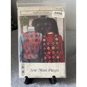 May include: A package for "Stained Glass Patches" sewing project. The package features images of vests with diamond patterns in red, blue, and brown. The text "Sew Mini Pieces" is printed on the bottom of the package.