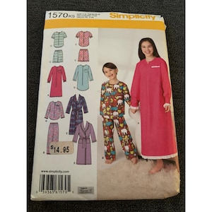 May include: Simplicity sewing pattern 1570K5 featuring sleepwear designs for children and adults. The pattern includes options for pajamas, nightgowns, and robes. The cover shows illustrations of the finished garments and a photo of a child and an adult wearing the sleepwear.
