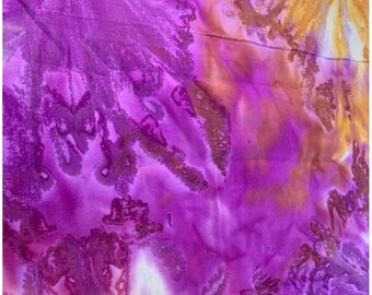 Puede incluir: Un tejido textil que presenta un vibrante patrón de teñido anudado con tonos magenta intenso, morado brillante y amarillo dorado cálido. Los colores se mezclan con formas orgánicas fluidas y bordes intrincados y difusos en la superficie.