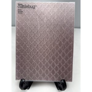 May include: A rectangular Cricut Cuttlebug embossing folder in a dusty mauve color. The surface features a repeating geometric mosaic pattern of interlocking quatrefoil shapes. The text Cricut cuttlebug and Mosaic are printed in the top left corner.