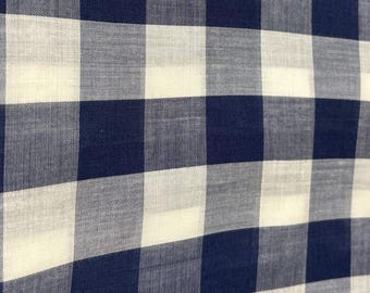 Puede incluir: Primer plano de una tela con un clásico estampado de cuadros vichy azul y blanco. El material tejido presenta una cuadrícula repetida de cuadrados grandes y de tamaño uniforme. La tela tiene un aspecto ligeramente texturizado.