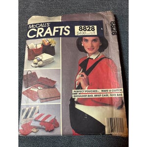 May include: Vintage McCall's Crafts pattern envelope featuring various pouch designs. The envelope showcases a woman in a red jacket and black bag. The text reads "Perfect Pouches - Make a Clutch, Shoulder Bag, Brief Case, Tote Bag."