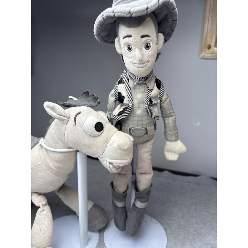 K&ouml;nnte beinhalten: Ein Pl&uuml;schtier eines Cowboy-Charakters mit passendem Pferd. Die Cowboy-Puppe tr&auml;gt einen Hut, eine Weste und Stiefel. Das Pferd ist hell gef&auml;rbt mit einem dunklen Sattel. Die Spielzeuge stehen auf einem wei&szlig;en St&auml;nder.