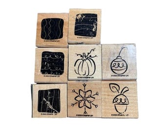 Peut inclure: Neuf tampons en bois avec divers motifs, dont une citrouille, un flocon de neige et un gland. Les tampons ont des motifs à l'encre noire sur un fond en bois clair. Le texte "© 2003 STAMPIN' UP!" est visible.