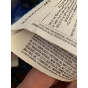 May include: Close-up of a white label with black text. The text reads: "MANUFACTURING PURPOSES/TA USAGE PRIVE/PRIVATE HOME USE/COMMERCIALES OU DE PRODUCTION EN SERIE/PARA USO COMERCIAL/FLEX UTILIZAR CON PROPOSITOS DE COMERCIALIZACION/2015 SIMPLICITY PATTERN CO. MFD FOR/FAB. 261 MADISON AVENUE, NEW YORK, NY 10016, USA/REVESBY NSW 2212, AUSTRALIA SIMPLICITY LTD, P.O. BOX 545 7WZ, UK. PRINTED IN/IMPRESO EN/IMPRIME/ALL RIGHTS RESERVED"
