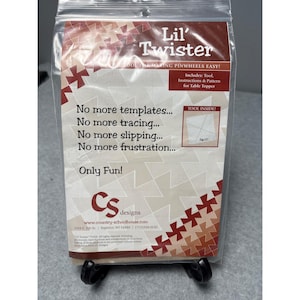 May include: A clear plastic package containing a quilting tool kit. The package features the text "Lil' Twister" and includes a tool, instructions, and a pattern for a table topper. The design includes a geometric pattern in shades of brown and white.