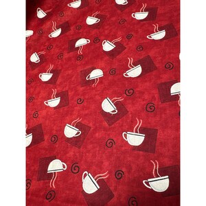 May include: Red fabric with a repeating pattern of white coffee cups with steam, set on dark red squares, and surrounded by brown swirls. The fabric has a textured appearance.