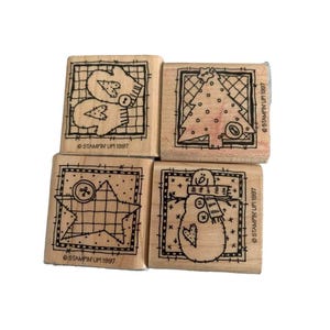 May include: Four wooden stamps with holiday-themed designs. The stamps feature a pair of mittens, a Christmas tree, a star with a button, and a snowman. Each stamp has a black border and the text "STAMPIN' UP! 1997".