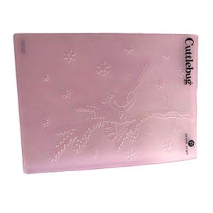 May include: A pink Cuttlebug embossing folder featuring a bird perched on a branch with snowflakes. The Provo Craft logo is visible. The folder is rectangular and has a slightly translucent appearance.