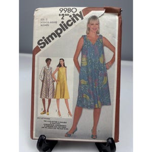 May include: A Simplicity 9980 sewing pattern envelope featuring illustrations of three sleeveless dresses. One dress is blue with a yellow and green tropical print, one is solid yellow, and one has a brown and white chevron pattern.