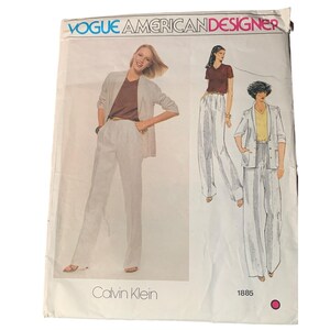 May include: A Vogue American Designer sewing pattern envelope for Calvin Klein design 1885. The front features illustrations of a blazer, trousers, and a v-neck top. The text reads Vogue American Designer, Calvin Klein, and the number 1885.
