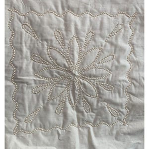 May include: A white fabric square with a white pearl bead embroidery design of a flower with eight petals.
