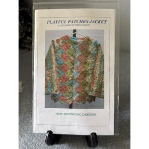May include: A sewing pattern for a "Playful Patches Jacket" made from a tee shirt. The jacket is displayed on a hanger. The jacket is made of colorful patches in shades of blue, green, and red. The text "New Beginning Designs" is at the bottom.