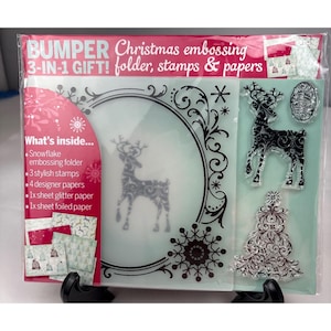 Puede incluir: Un set de regalo Bumper Christmas 3 en 1 que contiene una carpeta de relieve, tres sellos y cuatro papeles de diseño. El empaque presenta texto, una carpeta de relieve de copo de nieve con un diseño de reno y sellos transparentes.