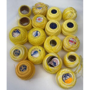 May include: A collection of yellow crochet thread spools and balls. The thread is in various sizes and packaging, with some spools showing labels with text and brand names. The color is a bright, sunny yellow.