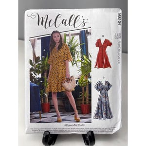 May include: A McCall's sewing pattern, M8104, featuring a woman in a yellow dress with a floral pattern. The pattern includes multiple view options and simple instructions. The size is F5 (16-18-20-22-24). The hashtag #DawnMcCalls is visible.