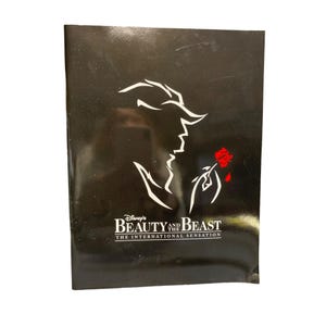 May include: Black cover featuring a white silhouette of the Beast and a red rose. The Disney's Beauty and the Beast logo is below the image, with the text "THE INTERNATIONAL SENSATION".