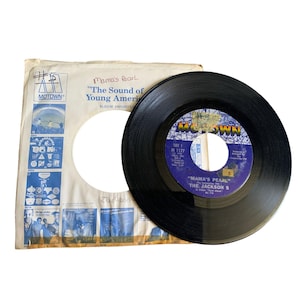 May include: A vintage black vinyl record from The Jackson 5, titled "Mama's Pearl," with a blue and white Motown label. The record is next to its original paper sleeve, which has the Motown logo and album details.