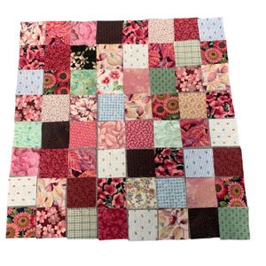 May include: A patchwork quilt composed of numerous fabric squares in various shades of pink, red, and brown. The squares feature floral and patterned designs, including sunflowers, leaves, and small polka dots. The quilt is a mix of textures and colors.