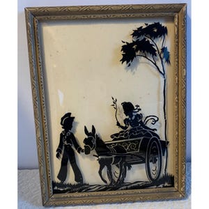 May include: Vintage framed silhouette art. The artwork depicts a black silhouette scene of a person leading a donkey pulling a cart with a person seated inside. A tree is on the right side. The frame is gold-toned.