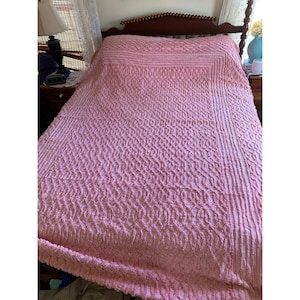 May include: A pink quilted bedspread with a diamond pattern. The bedspread is made of a soft, textured fabric.