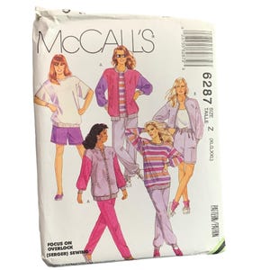 Peut inclure: Une enveloppe de patron de couture McCall's vintage avec des illustrations de vêtements de sport pour femmes. L'enveloppe est blanche avec le logo McCall's et le numéro de modèle 6287. Les illustrations montrent des tenues roses, violettes et blanches.