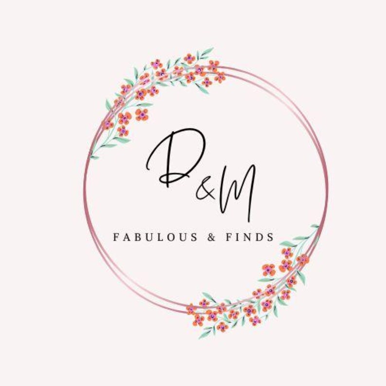 K&ouml;nnte beinhalten: Ein Logo mit einem doppelten rosa Kreis, den Buchstaben "D&M" in eleganter schwarzer Schrift und den Worten "FABULOUS & FINDS" darunter. Florale Akzente mit orangefarbenen Bl&uuml;ten und gr&uuml;nen Bl&auml;ttern schm&uuml;cken den Kreis.