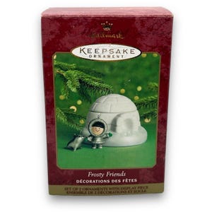 May include: A Hallmark Keepsake Ornament box featuring a winter scene. The box displays a ceramic igloo, a small figurine of a person in winter attire, and a small seal. The text "Frosty Friends" and "DÉCORATIONS DES FÊTES" are visible.