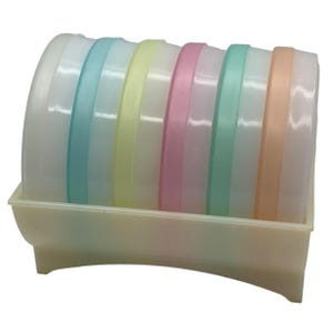 May include: A set of pastel-colored plastic bowls with lids, arranged in a matching tray. The bowls feature bands of light blue, yellow, pink, and orange. The tray and bowls are made of a translucent plastic.