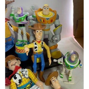 May include: A collection of Toy Story character action figures, including Woody, Buzz Lightyear, and others. The figures are brightly colored and made of plastic, with detailed designs. The figures are standing in a group, with some figures in the foreground and others in the background.