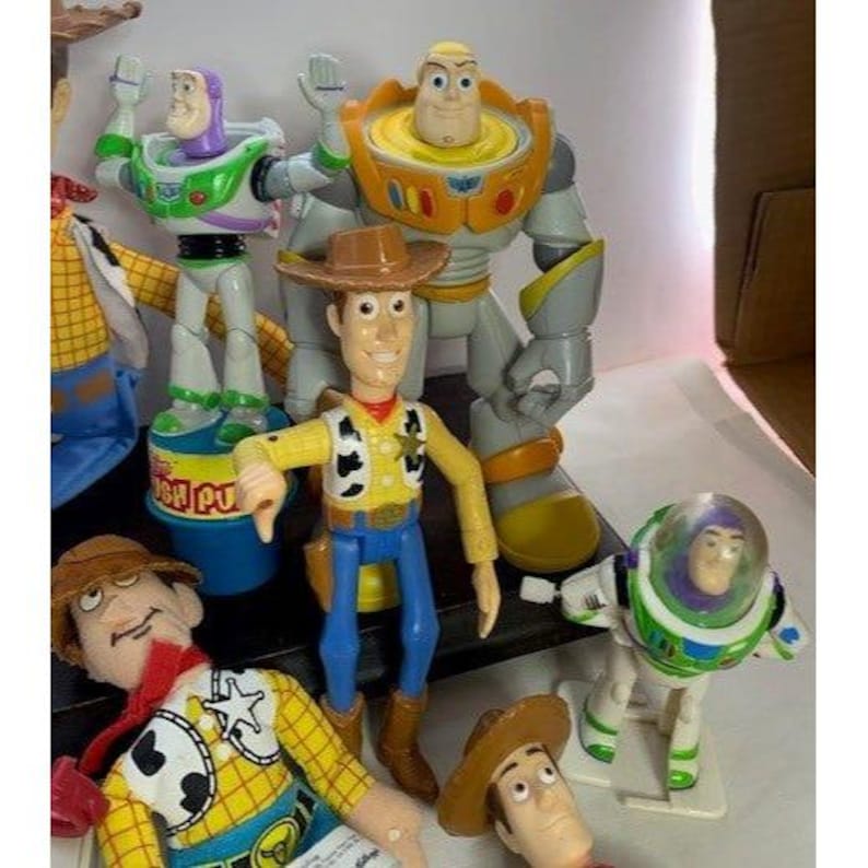 May include: A collection of Toy Story character action figures, including Woody, Buzz Lightyear, and others. The figures are brightly colored and made of plastic, with detailed designs. The figures are standing in a group, with some figures in the foreground and others in the background.