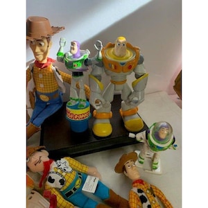 May include: A collection of Toy Story character figurines, including Woody and Buzz Lightyear. The figures are in various poses and sizes, with detailed paintwork and recognizable features. The toys are made of plastic and are likely for children.