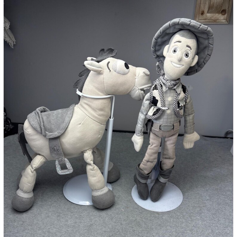 K&ouml;nnte beinhalten: Ein Pl&uuml;schtiersatz mit einer Cowboy-Puppe und einem Pferd. Die Cowboy-Puppe tr&auml;gt einen Hut, eine Weste und Stiefel. Das Pferd hat einen Sattel und wird von einem St&auml;nder gehalten. Beide Spielzeuge sind haupts&auml;chlich grau und beige.