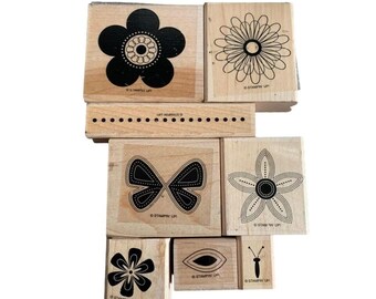 Peut inclure: Un ensemble de tampons en bois avec des motifs floraux et papillons. Les tampons ont des motifs à l'encre noire sur un fond en bois naturel. L'ensemble comprend diverses formes de fleurs, un papillon et un petit tampon avec un papillon.