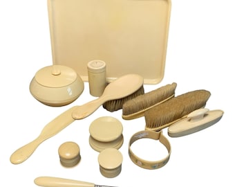 May include: A collection of cream-colored vanity accessories including a rectangular tray, a lidded jar, a hairbrush, two clothes brushes, a shoehorn, a button hook, two small containers, a circular stand, and a ring with a floral pattern.