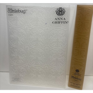 May include: A clear, plastic Cricut Cuttlebug embossing folder with a repeating circular floral design. The folder is labeled "Anna Griffin" and "Cuttlebug". A matching brown folder is also present.