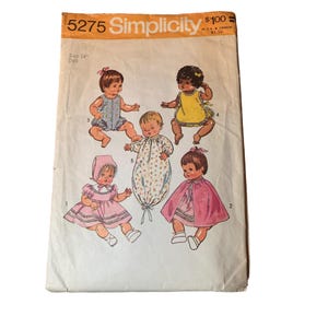 May include: Vintage Simplicity sewing pattern number 5275 for a 14 inch doll. The pattern includes five different outfits: a pink dress with a cape, a pink and white dress with a bonnet, a white and blue gingham dress, a yellow bib, and a floral print sleeping bag.