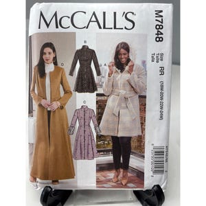 May include: McCall's M7848 sewing pattern featuring coat designs. The pattern includes illustrations of various coat styles, including a long camel-colored coat, a black textured coat, and a plaid coat with a hood. The size range is 18W-24W.