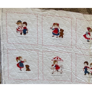 May include: White fabric with red stitched squares featuring children and text. The fabric has a repeating pattern of red hearts. The text includes "Love Makes The World Go Round" and phrases like "A little sharing can mean a lot..."
