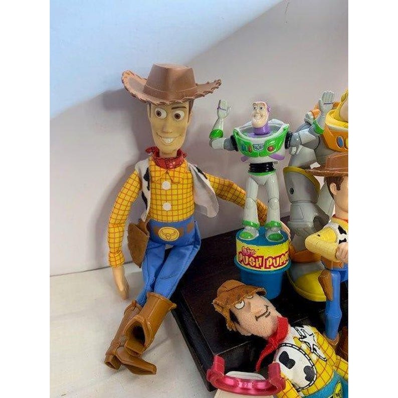 May include: A collection of Toy Story character figurines, including Woody in a cowboy hat, yellow shirt, blue pants, and brown boots. Buzz Lightyear is also present, along with other characters. The toys are brightly colored and detailed.