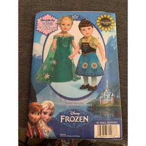 May include: Simplicity sewing pattern 1088 for making 18-inch doll clothes. The pattern features a green and blue dress with a cape and a brown and blue dress with a vest. The pattern is for Disney Frozen.