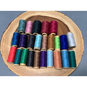 May include: A collection of 20 spools of thread in various colors, including red, green, blue, purple, and brown. The spools are arranged in a circle on a wooden surface.