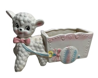 May include: A vintage ceramic lamb planter, white with a pink bow tie and blue accents. The lamb pulls a white cart with pink and blue decorative elements. A charming, decorative piece.